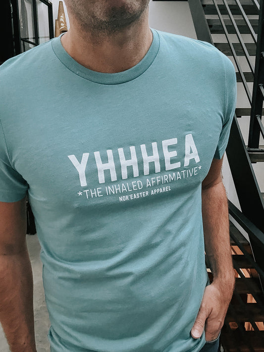 Person wearing a teal t-shirt with 'YHHHEA' text design.