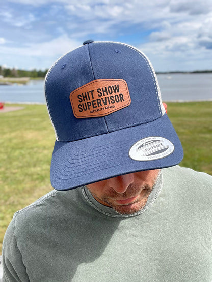 black nor'easter hat front view with a faux leather patch saying shit show supervisor