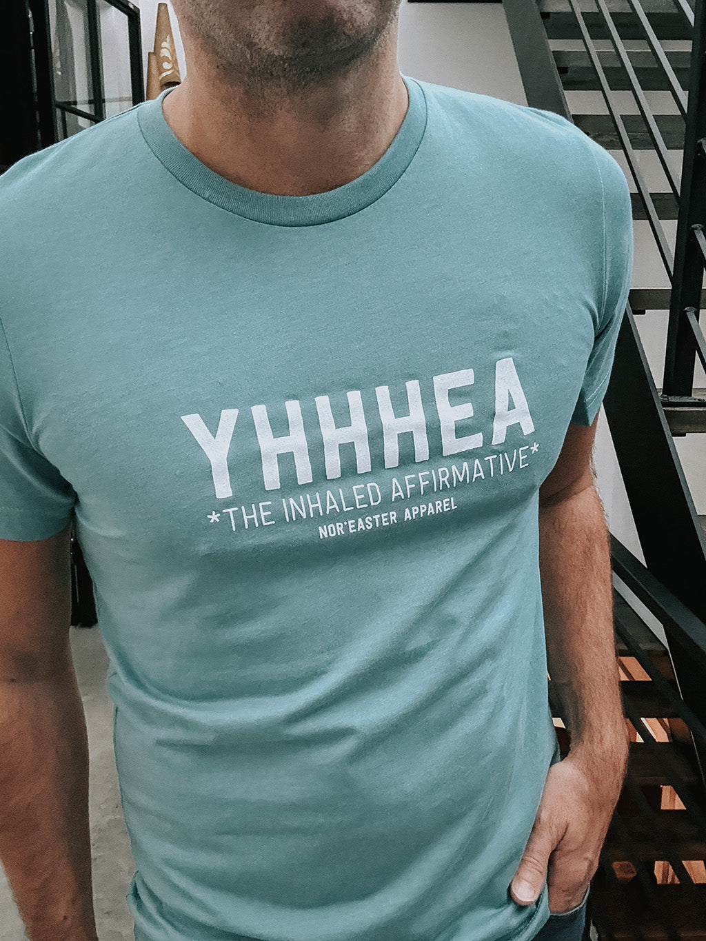 Person wearing a teal t-shirt with 'YHHHEA' text design.