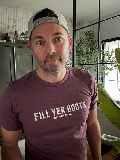 Man wearing a maroon t-shirt with 'Fill Yer Boots' text indoors.